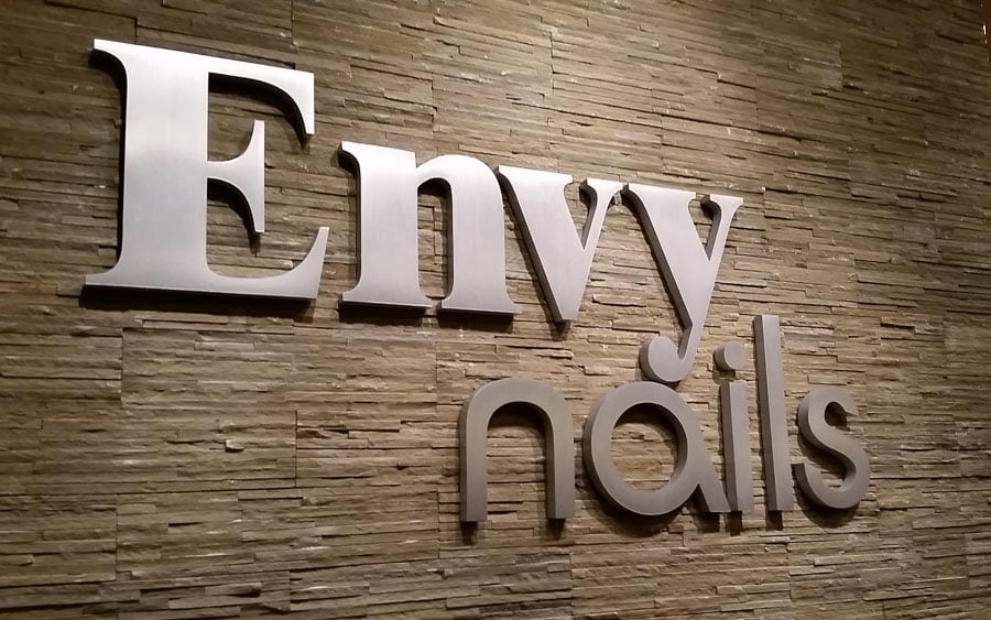 thick brushed cast aluminum letters for nail salon mounted inside lobby on stone wall