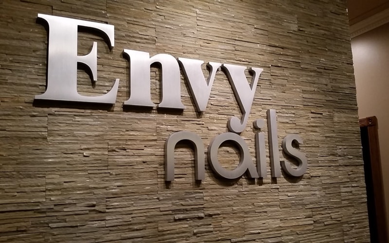 thick brushed cast aluminum letters for nail salon mounted inside lobby on stone wall